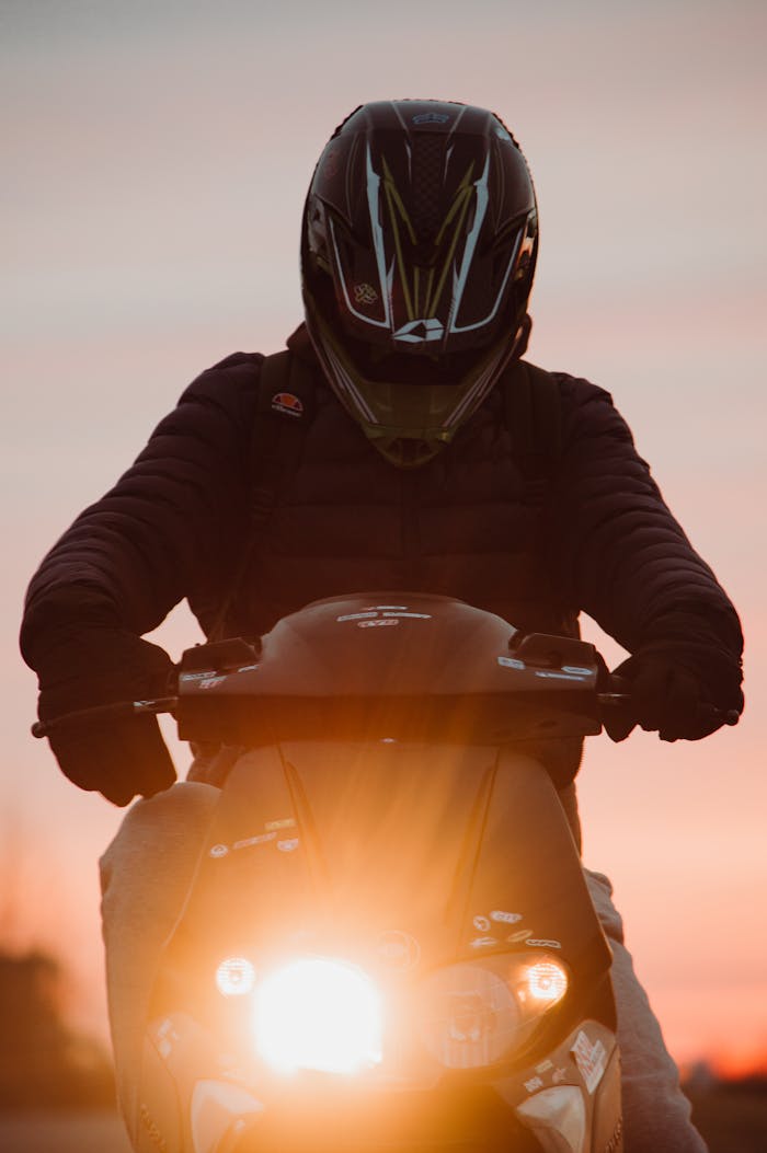 Silhouetted motorcyclist riding at sunset in Lithuania with headlight on.