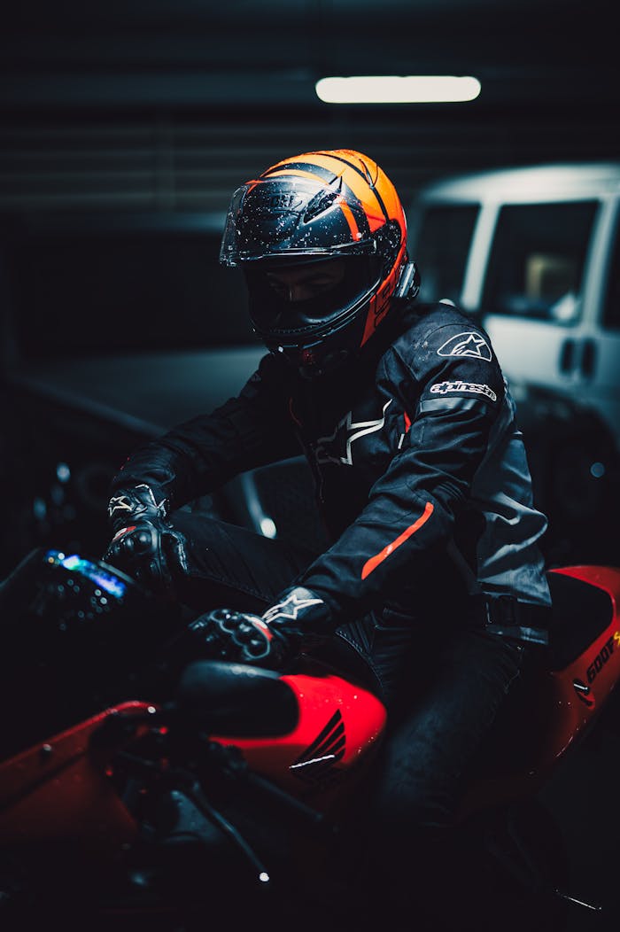 Motorcyclist wearing helmet on red bike in dimly lit garage.