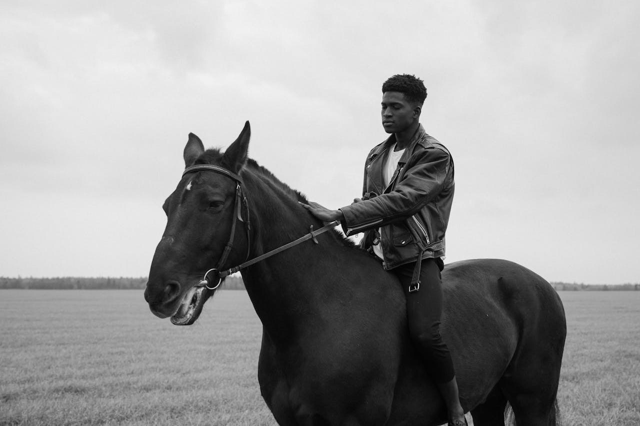 A monochrome image of a man riding a horse in a field.